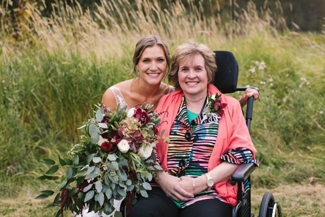 Alli holding a floral bouquet with her mom beside her in a wheelchair.