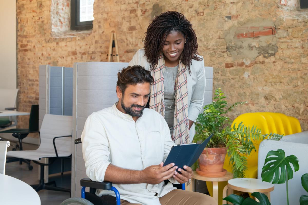 A man is sitting looking at a tablet with a woman looking at it over his shoulder.