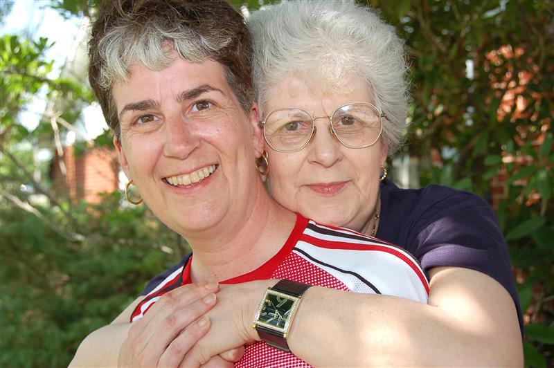 Two people hugging. Both have short hair. One is wearing a red cycling shirt and the other is wearing a purple t-shirt and glasses.