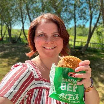 Caitlin smiling and holding a Teen Burger® outside with trees in the background